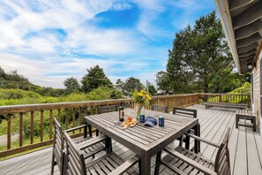 Una terraza de madera con una mesa lista para comer, rodeada de sillas, y vistas a un paisaje exuberante.