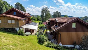 Un chalet en bois doté d’un toit à pente, d’un patio couvert et d’un petit jardin.