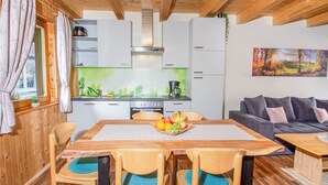 Une cuisine moderne avec des meubles blancs, un îlot central agrémenté d’un panier de fruits, et un coin repas avec des chaises et une table en bois.