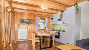 Une cuisine compacte équipée d’un réfrigérateur, d’une cuisinière et de meubles blancs. Une table à manger avec des chaises est placée devant une fenêtre ornée de rideaux.