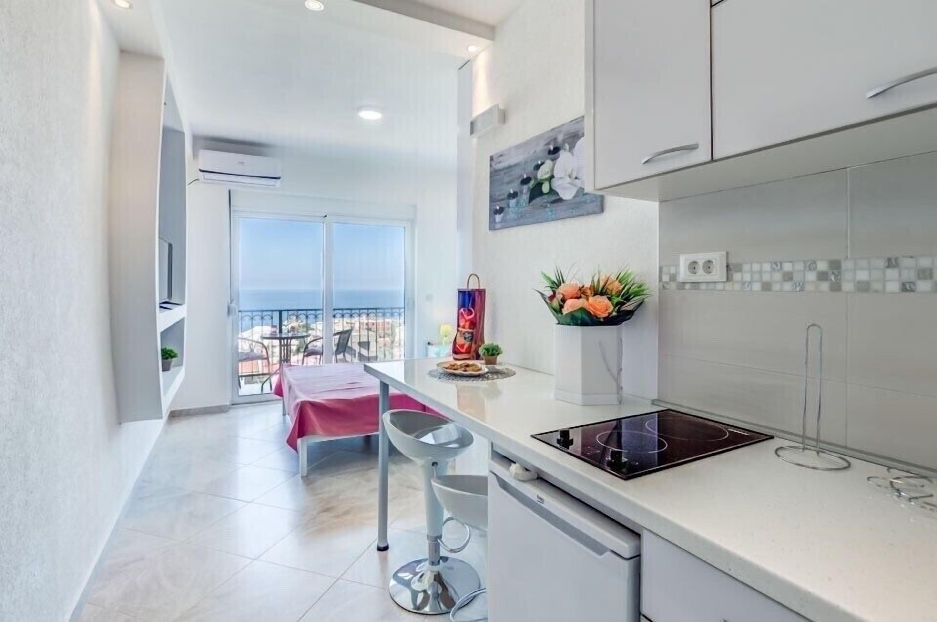 Una cocina moderna con una isla grande, un comedor con una mesa rosa y un balcón con vistas.