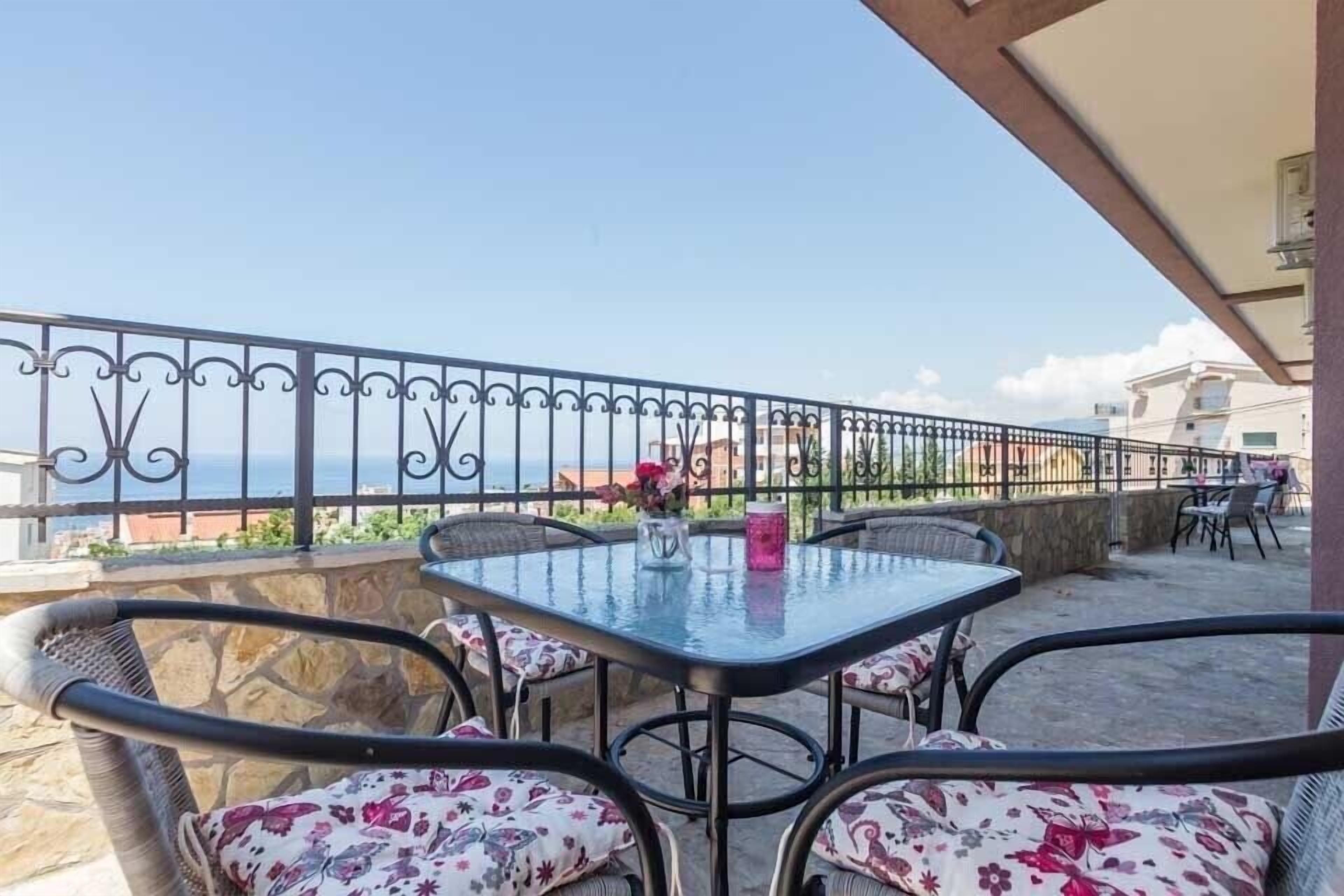 A terrace with a glass table and wicker chairs, overlooking a coastal view.
