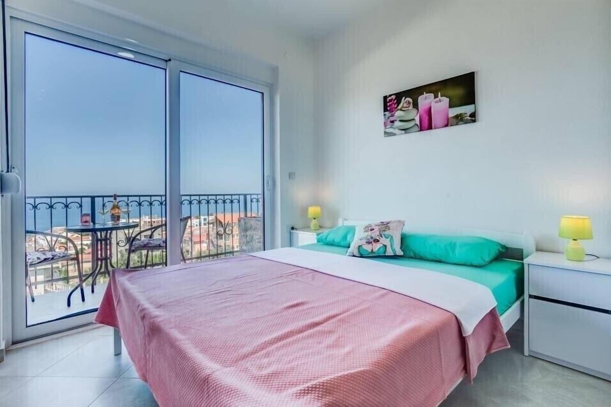 A bedroom with a bed, a nightstand, a bedside table, a window, and a balcony with a table and chairs.