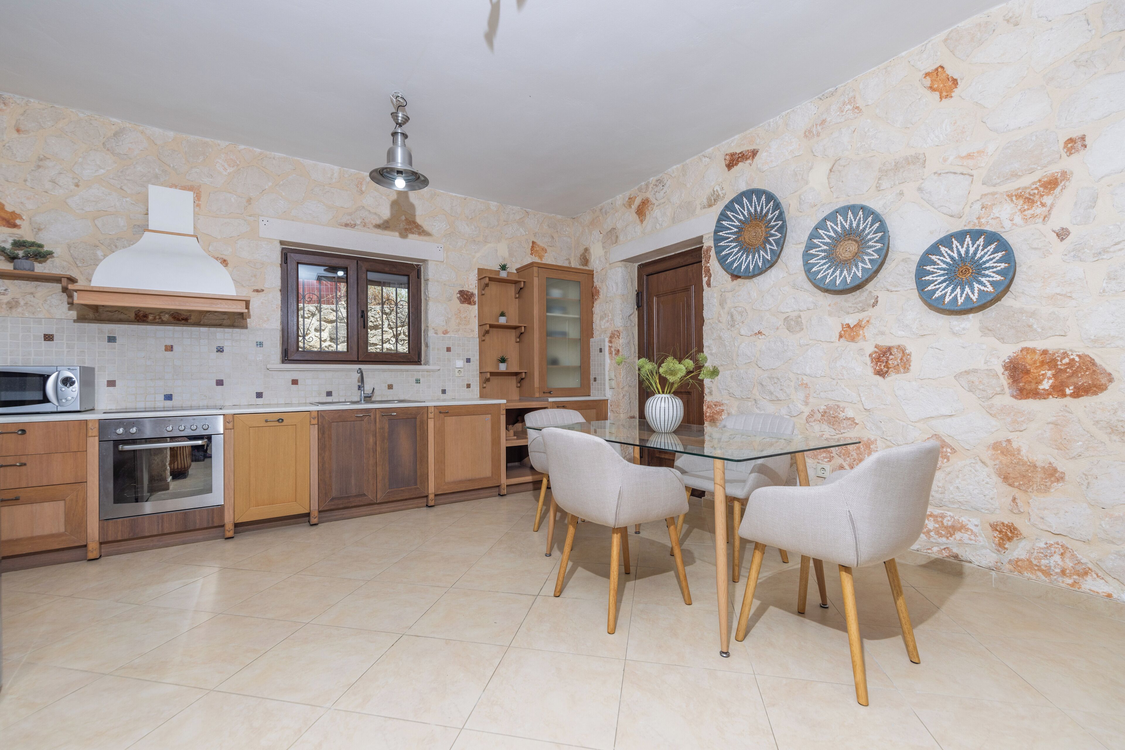 Een moderne keuken met een stenen muur, houten kasten, een ingebouwde oven en een eetgedeelte met een glazen tafel en stoelen.