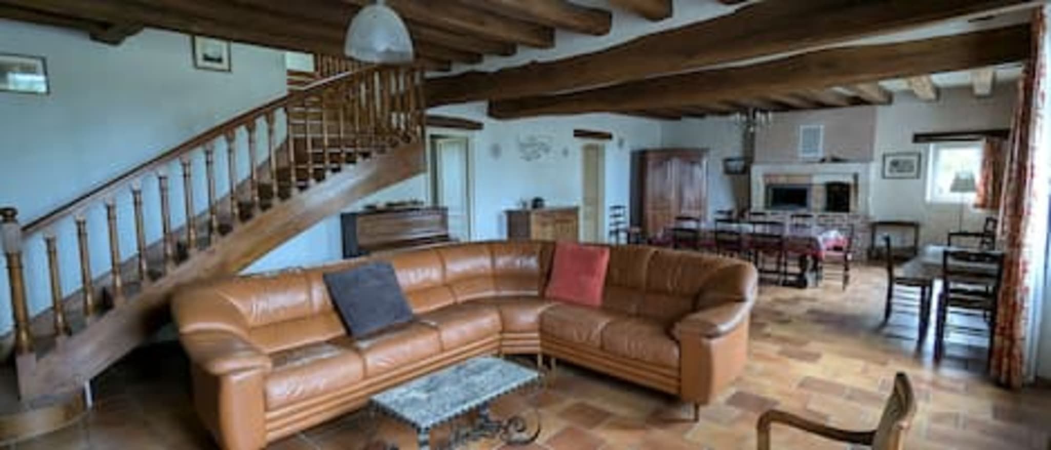 A spacious living room with a curved leather sofa, a wooden staircase, and a dining area with chairs and a table.