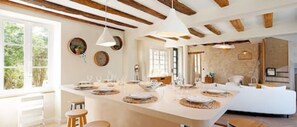 A spacious kitchen with a large island, wooden beams on the ceiling, and a view of the outdoors. - Le Refuge Une Parenthèse en Pleine Nature (Neuillé-Pont-Pierre)
