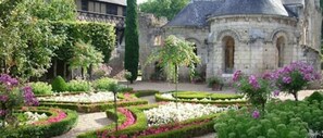 Ein Garten mit ordentlich geschnittenen Hecken und blühenden Pflanzen vor einem historischen Gebäude mit einer Kuppel.