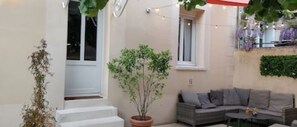 Eine Terrasse mit einer grauen Couch, einem Blumentopf und einer weißen Tür.