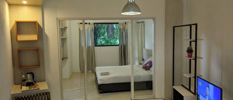 A modern bedroom with a bed, a TV, and a sliding door leading to a balcony.