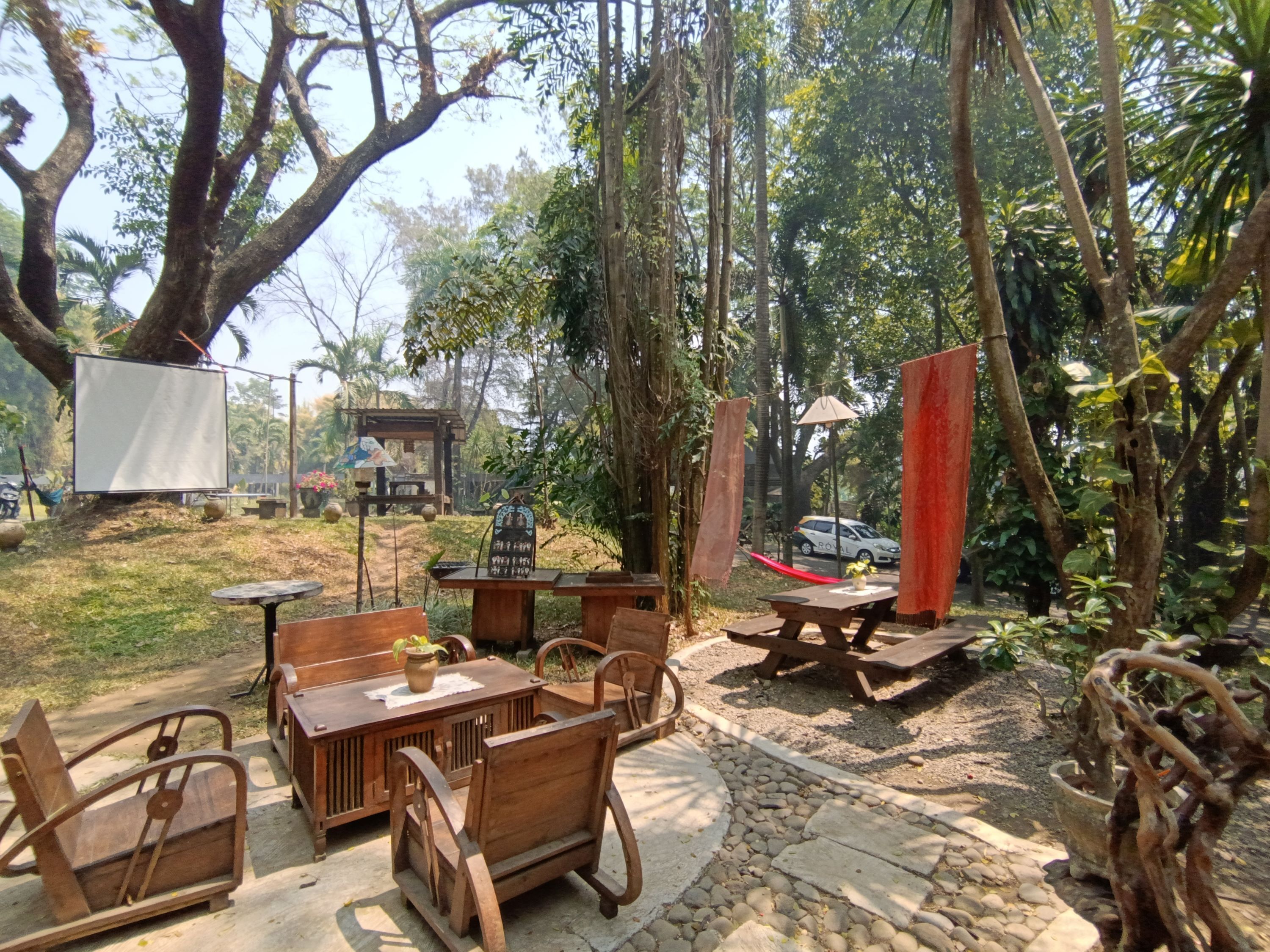 An outdoor seating area with wooden furniture, a stone pathway, and a car parked in the background.