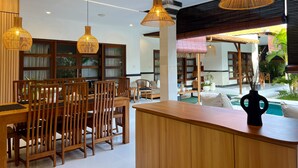 Ein modernes Interieur mit Holzmöbeln, hängenden Korblampen und Blick auf einen Pool.