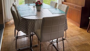 Et spiseområde med et rundt bord, stole, en hængende lampe og en reol.