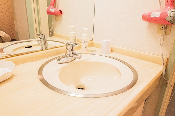Une salle de bain équipée d’un lavabo, d’un miroir et de deux sèche-cheveux roses fixés au mur.