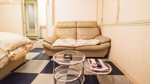 Et lille, kompakt hotelværelse med gulv i skakmønster, en enkelt sofa, et glashotelbord og en seng.