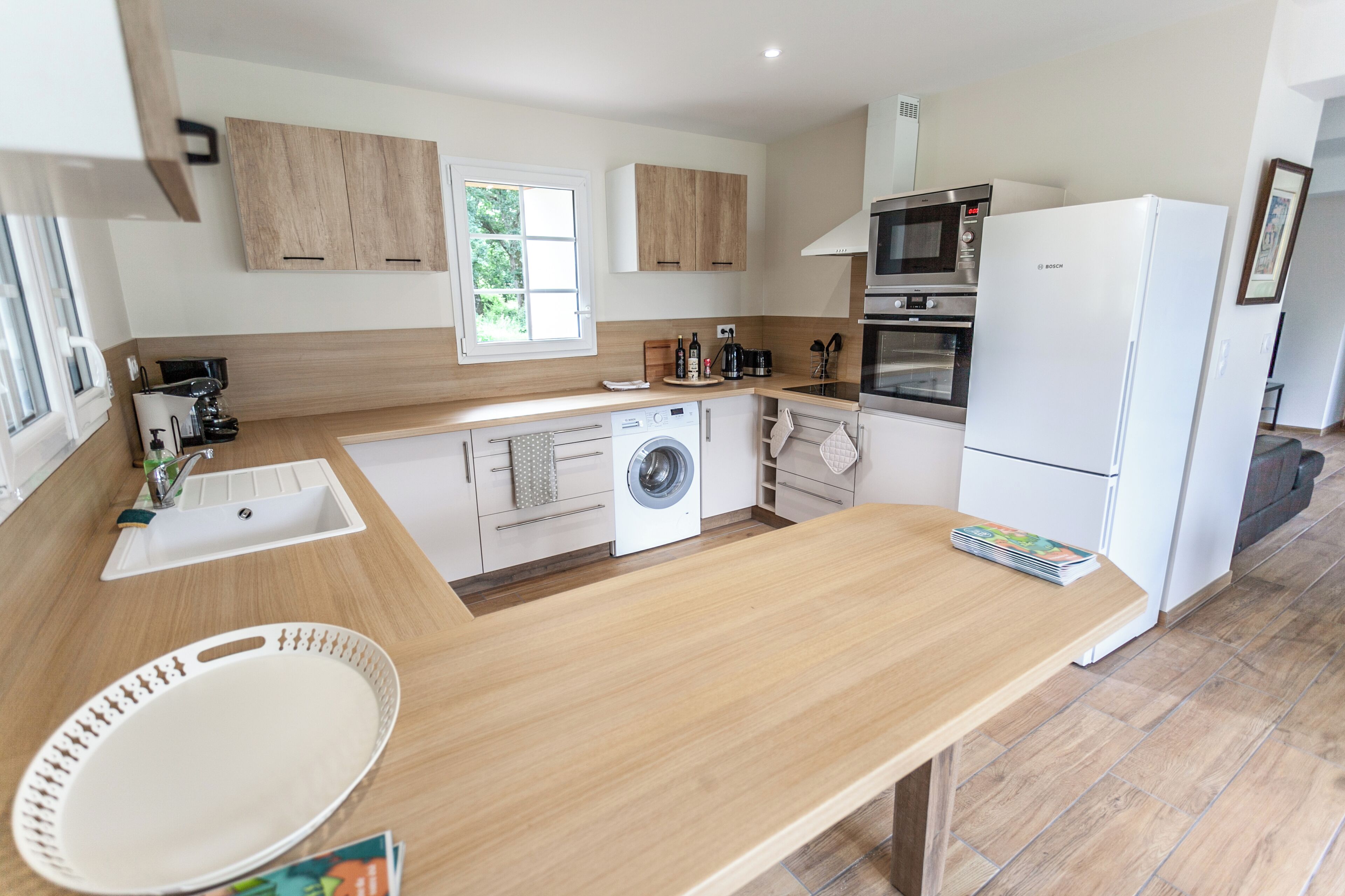 Une cuisine moderne avec des meubles en bois, un lave-linge encastré et un grand plan de travail.