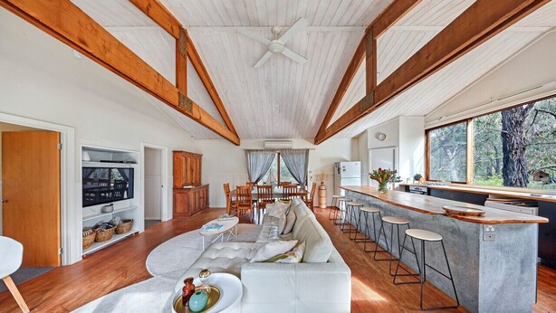 A spacious living area with a large sofa, a dining table, and a kitchen with a bar. - Rustic Treehouse - Aireys Inlet (Aireys Inlet)