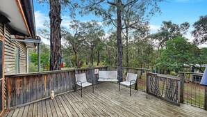 A wooden deck with metal chairs and a bench, surrounded by trees and a fence. - Rustic Treehouse - Aireys Inlet (Aireys Inlet)