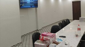 A conference room with a long table, chairs, a television on the wall, ceiling fans, and a patterned carpet. - Hotel Sunrise Ecostay  (New Delhi)