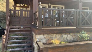 A wooden staircase leading to a deck with a stone planter and a small tree.