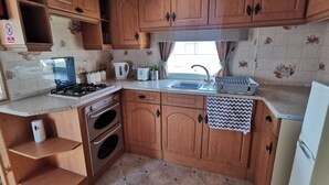Une cuisine de taille réduite, avec des meubles de rangement en bois, une cuisinière à gaz, un évier et un petit four.