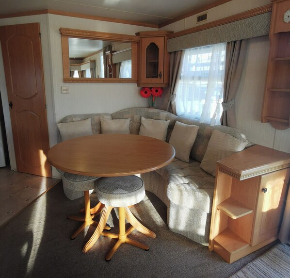 A cozy RV interior with a round wooden table, cushioned seating, a mirror, and a cabinet. - Plum 2 Coral Beach Ingoldmells 3 bed 6 Berth (Skegness)