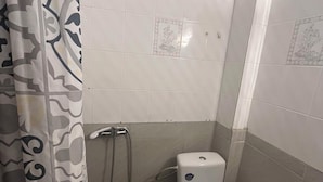 A small bathroom with a toilet, a shower, and a patterned curtain. - Sirtaki Apartments (Kassandra)