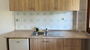 A compact kitchen with wooden cabinets, a built-in sink, and a small refrigerator. - Sirtaki Apartments (Kassandra)