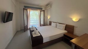 A hotel room with a bed, a TV, a bedside table, and a window with curtains. - Sirtaki Apartments (Kassandra)