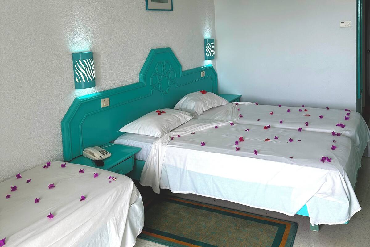 A hotel room with two single beds, a teal headboard, white bedding, a small bedside table with a phone, and a picture on the wall.