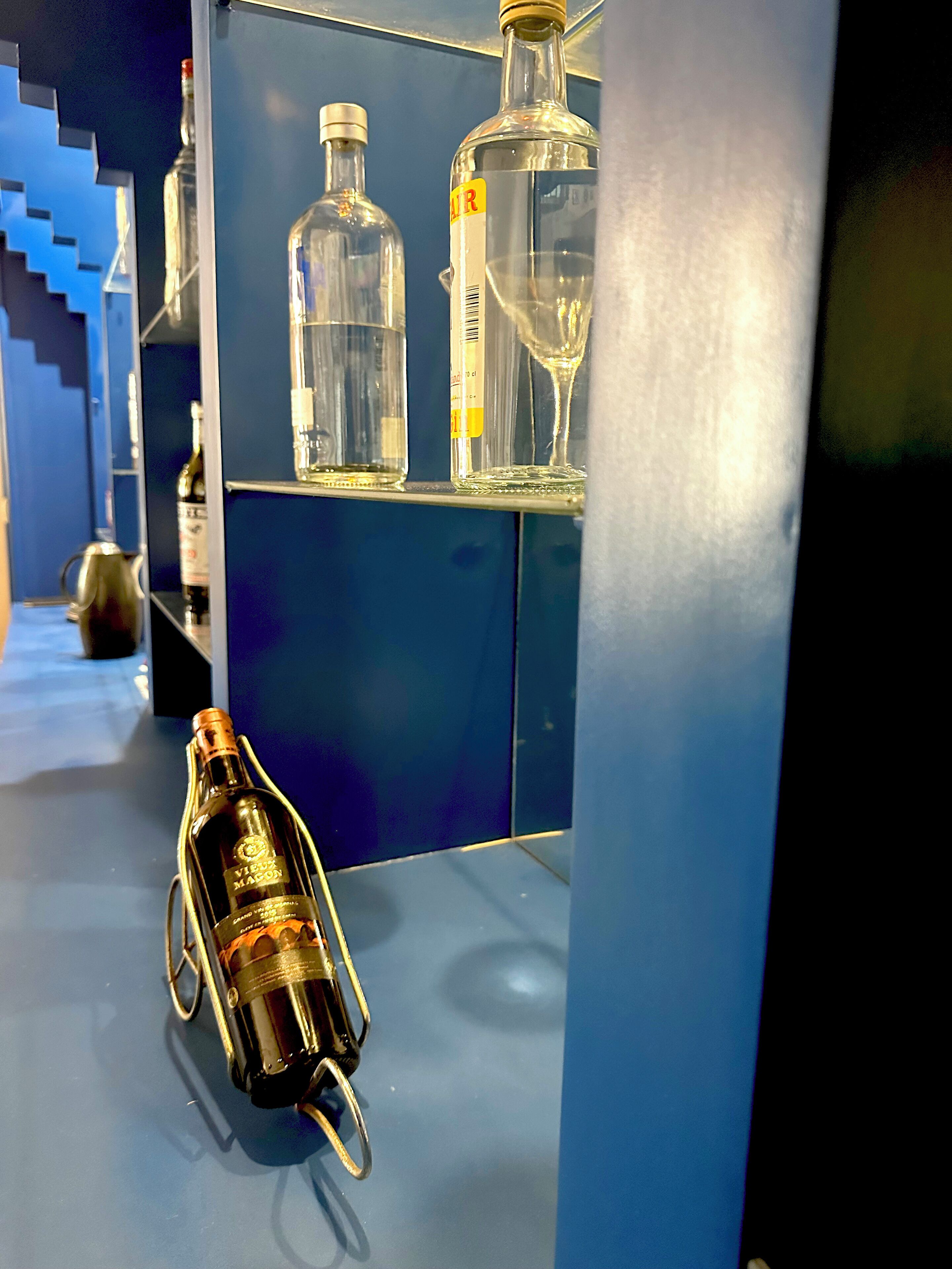 A bar area with various bottles and a wine glass on shelves.