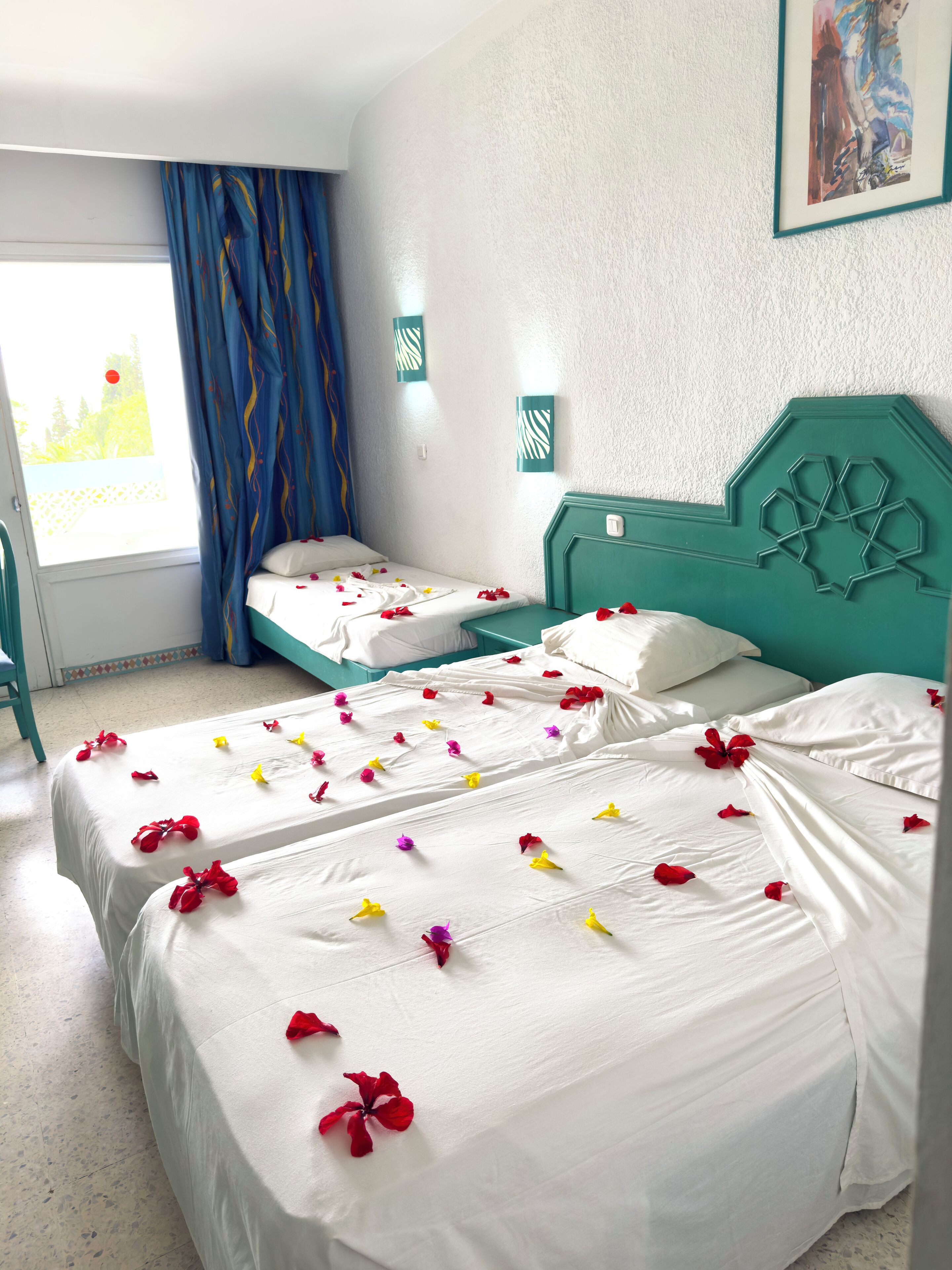 A hotel room with two beds, a window with curtains, and a painting on the wall.