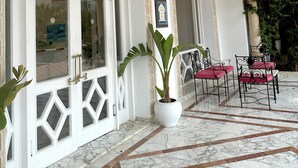 A spacious indoor area with white walls, large arched doorways, and a marble floor. There are potted plants and a table with chairs. - Green Golf Hammamet (Hammamet)