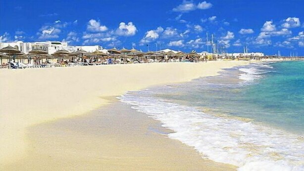 A beach with white sand, clear turquoise water, and a row of beach umbrellas. - Green Golf Hammamet (Hammamet)