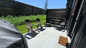 Un patio al aire libre con sillas Adirondack y una zona de parrilla cubierta.