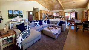 A spacious living room with a large sectional sofa, a wooden ceiling, and a view into the kitchen. - Beautiful Log Style Home in Eagle Mountain Estates, Big Bear Lake.  (Big Bear Lake)