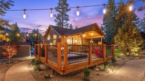A wooden cabin with a fenced deck, surrounded by trees and a gravel path. - Beautiful Log Style Home in Eagle Mountain Estates, Big Bear Lake.  (Big Bear Lake)