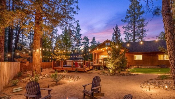 A cozy outdoor seating area with Adirondack chairs and a fire pit, surrounded by a wooden deck and string lights. - Beautiful Log Style Home in Eagle Mountain Estates, Big Bear Lake.  (Big Bear Lake)