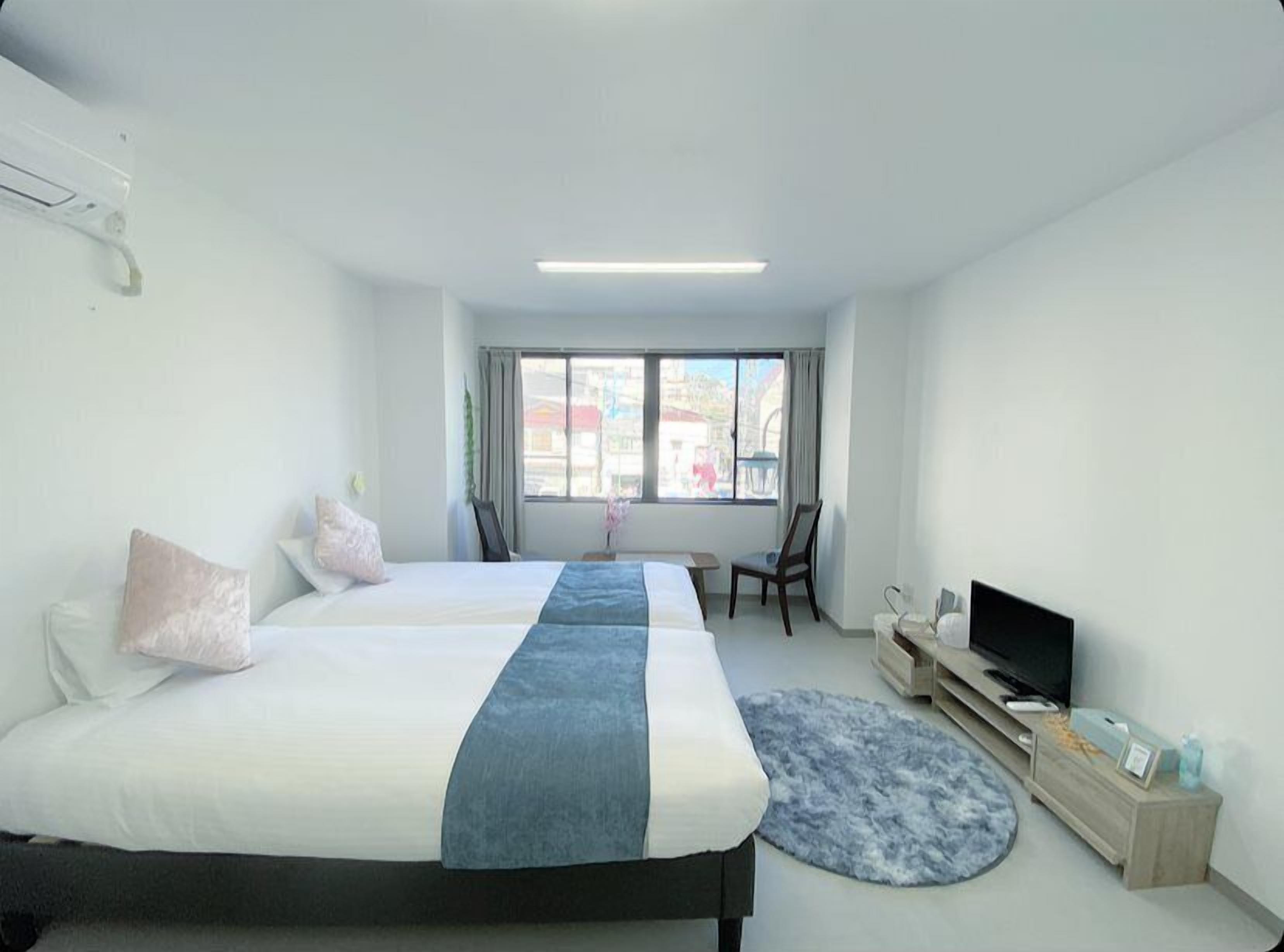 Moderni hotellihuone, jossa on kaksi sänkyä, televisio, työpöytä ja ikkuna, josta avautuu näkymä kaupunkiin.