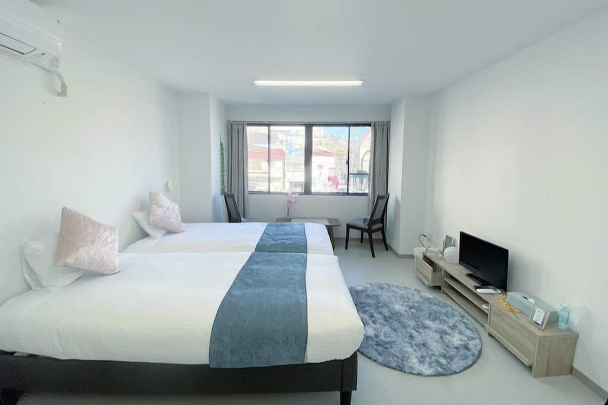 A modern hotel room with two beds, a TV, a desk, and a window with a view of the city.