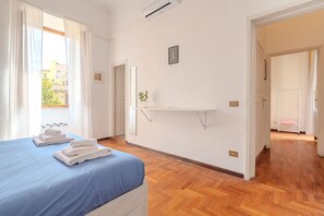 A hotel room with a bed, a window with curtains, a wall-mounted shelf, and a door leading to another room. - Casa Lucrezio Prati Saint Peter's Church (Roma)
