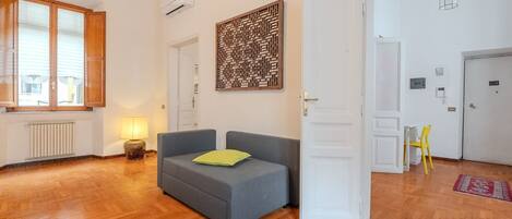 Ein Zimmer mit grauem Sofa, Holzboden, Wandpaneel und weißer Tür.