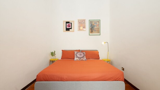 Ein Schlafzimmer mit einem Bett, zwei Nachttischen, einer Stehlampe und drei gerahmten Bildern an der Wand.