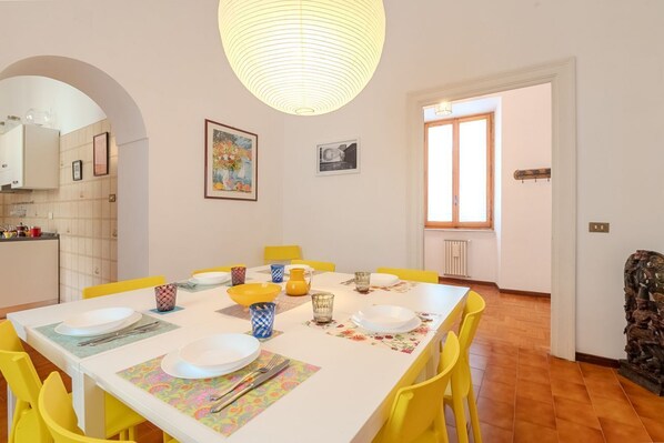 Un coin repas avec une table blanche, des chaises jaunes et un luminaire suspendu.