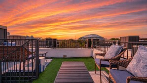 A rooftop terrace with outdoor furniture, a small grassy area, and a view of a dome-shaped building. - Luxury Stay | Short Walk to AT&T Stadium + Parking (Arlington)