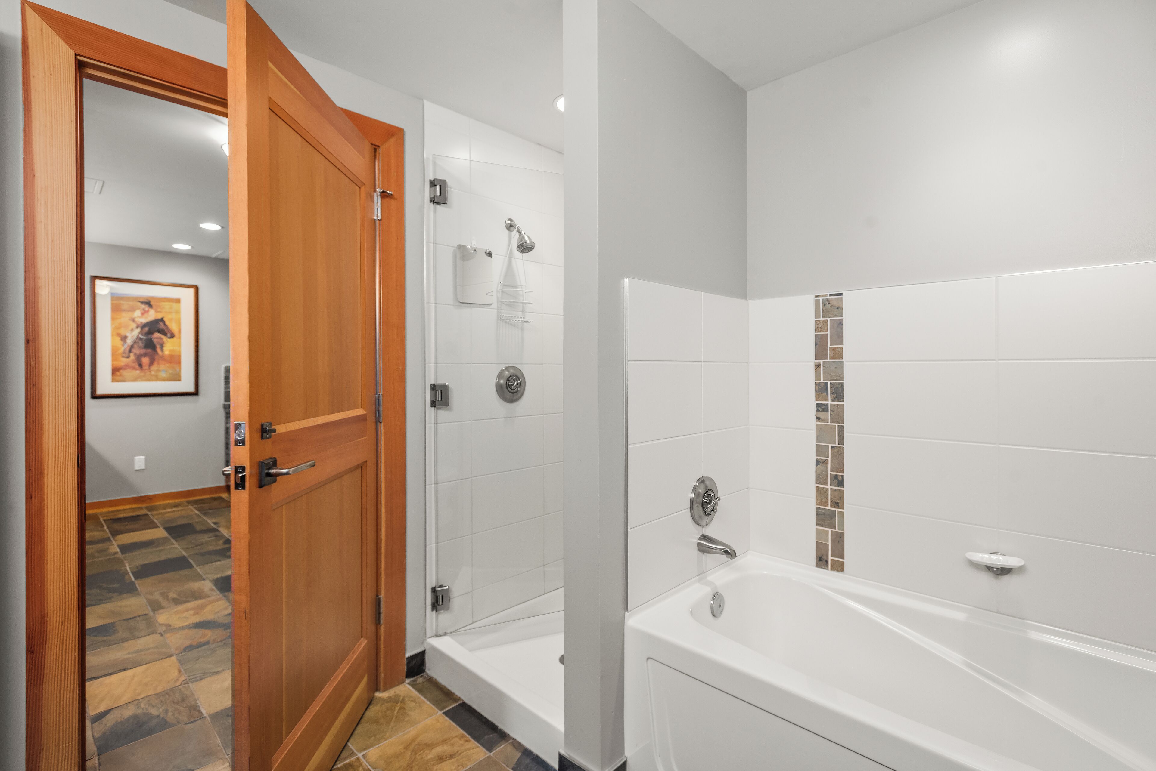 A modern bathroom with a shower, a bathtub, and a wooden door.