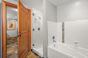 A modern bathroom with a shower, a bathtub, and a wooden door.