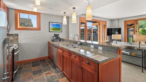 A modern kitchen with granite countertops, wooden cabinets, and a large island. There are pendant lights, a built-in oven, and a dishwasher. - Gondola Grove | Capitol Peak Lodge #3310 | 2B/2B (Snowmass Village)