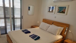 Een netjes opgemaakt bed met witte en blauw gestreepte handdoeken, een houten hoofdbord, nachtkastjes met lampen en twee ingelijste foto’s aan de muur.