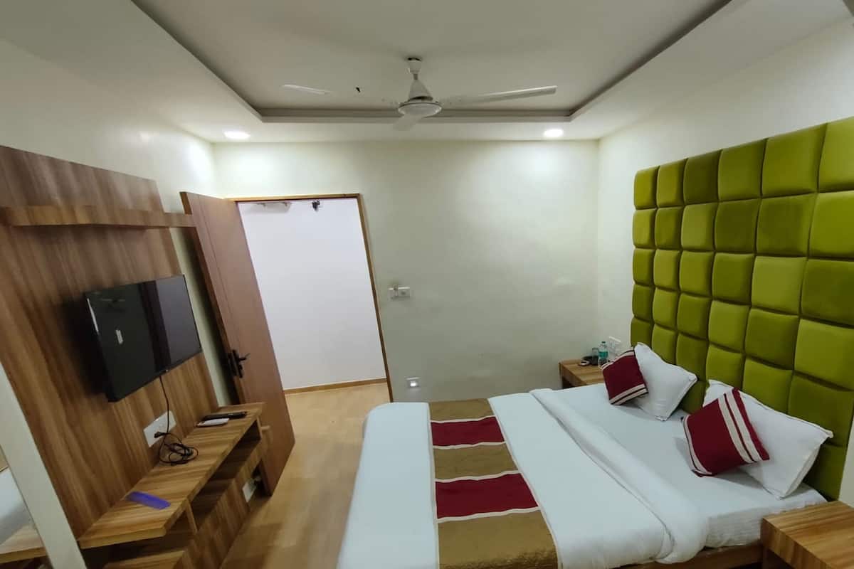 A modern hotel room with a bed, wooden side table, and a flat-screen TV.
