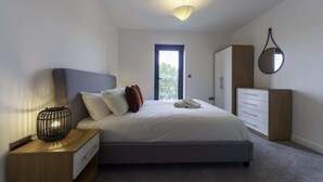 Ein modernes Schlafzimmer mit Bett, Nachttisch, Kleiderschrank und einem Fenster.
